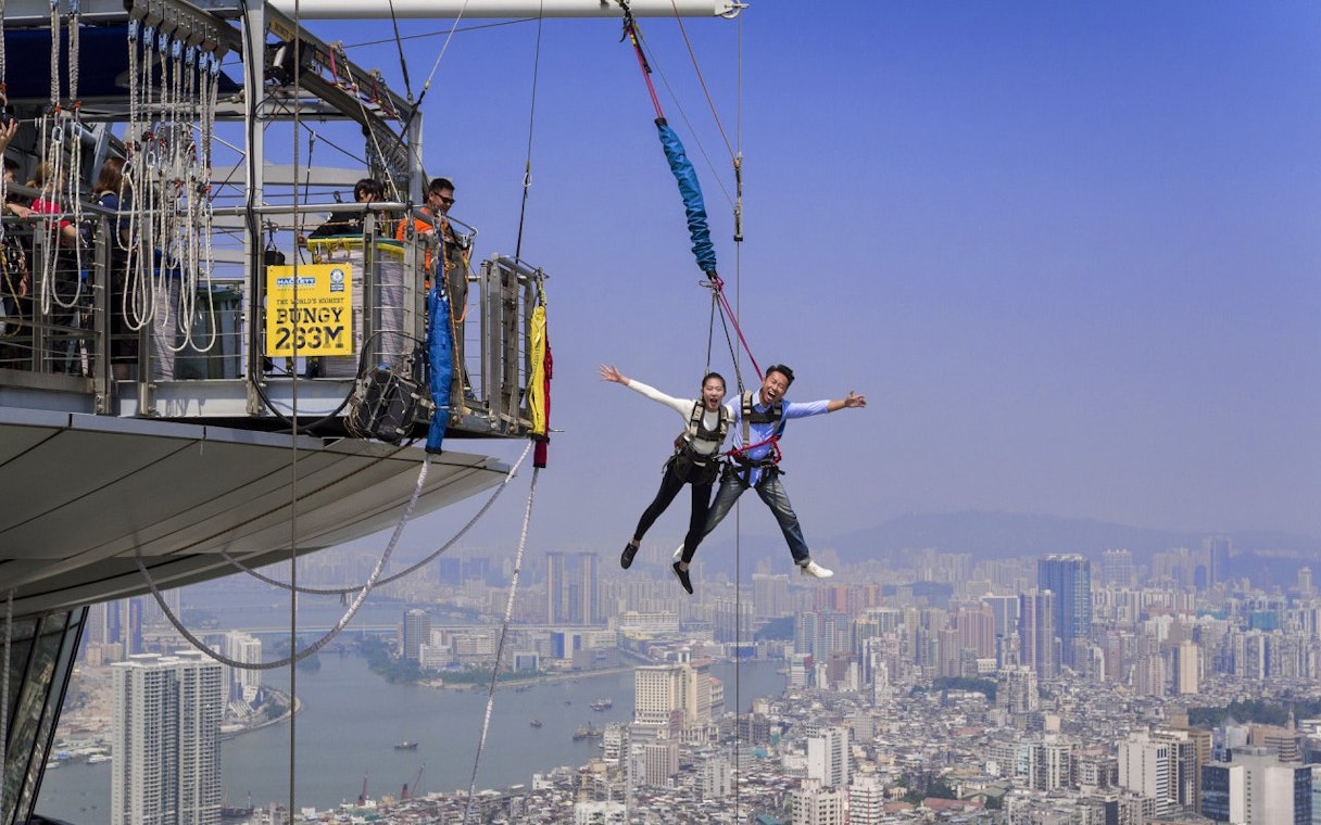 Couple bungee jumping at Skypark Macau with city skyline in the background.