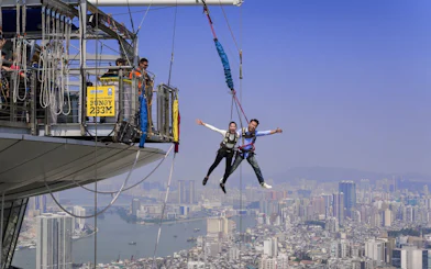 Couple bungee jumping at Skypark Macau with city skyline in the background.