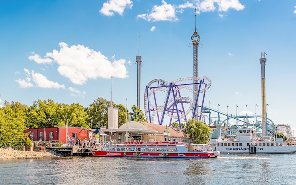 Stockholm sightseeing boat near amusement park rollercoaster on a sunny day.