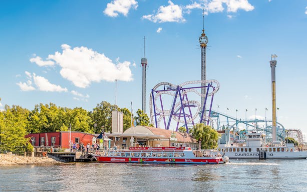 Stockholm sightseeing boat near amusement park rollercoaster on a sunny day.