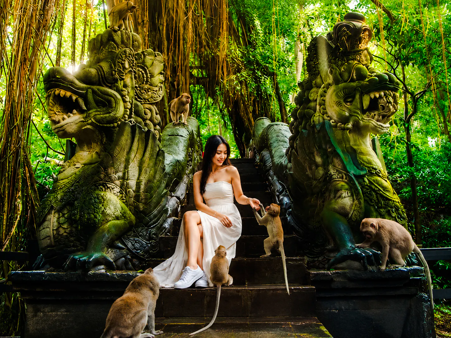 Woman interacting with monkeys on stone steps flanked by dragon statues in Ubud, Bali.