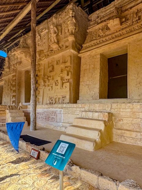 Ek Balam archaeological site with ancient stone carvings and steps under a thatched roof.