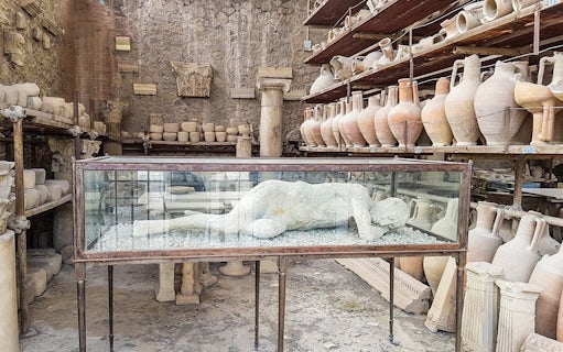 Plaster cast of a Pompeii inhabitant in a glass case surrounded by ancient pottery.
