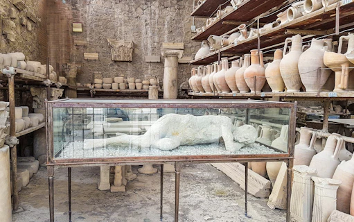 Plaster cast of a Pompeii inhabitant in a glass case surrounded by ancient pottery.