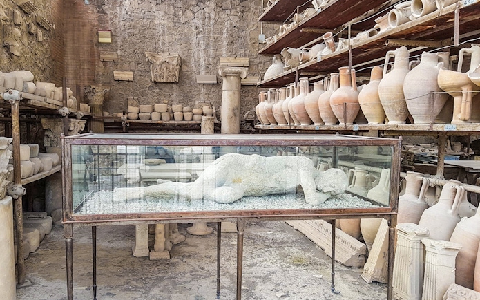 Plaster cast of a Pompeii inhabitant in a glass case surrounded by ancient pottery.