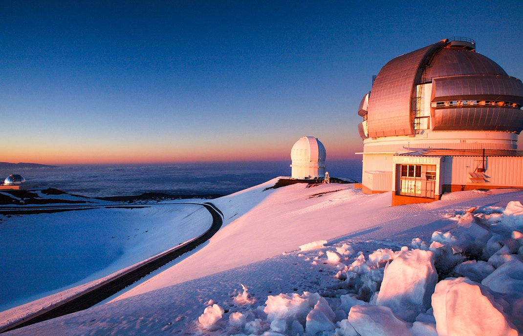 Snowy Mauna Kea Observatory domes at sunset in Hawaii.