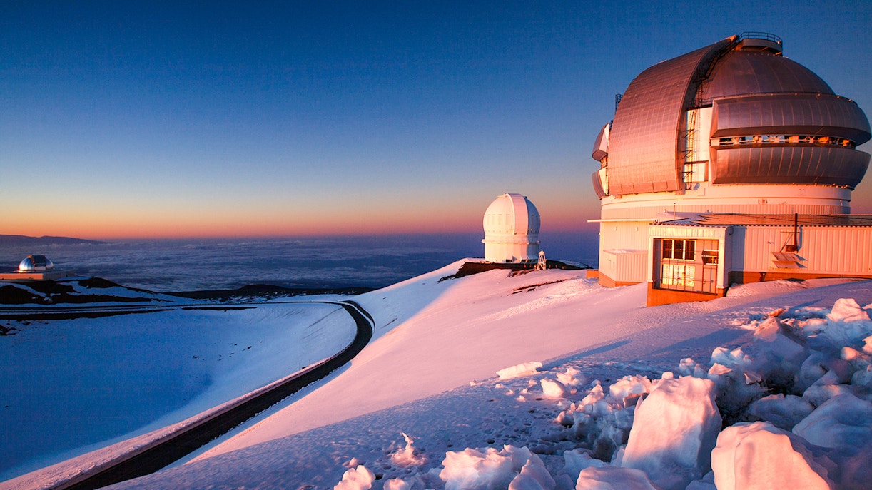 Snowy Mauna Kea Observatory domes at sunset in Hawaii.
