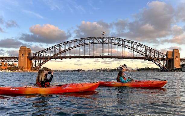 Kayakers paddle on Sydney Harbour with Sydney Harbour Bridge in the background.