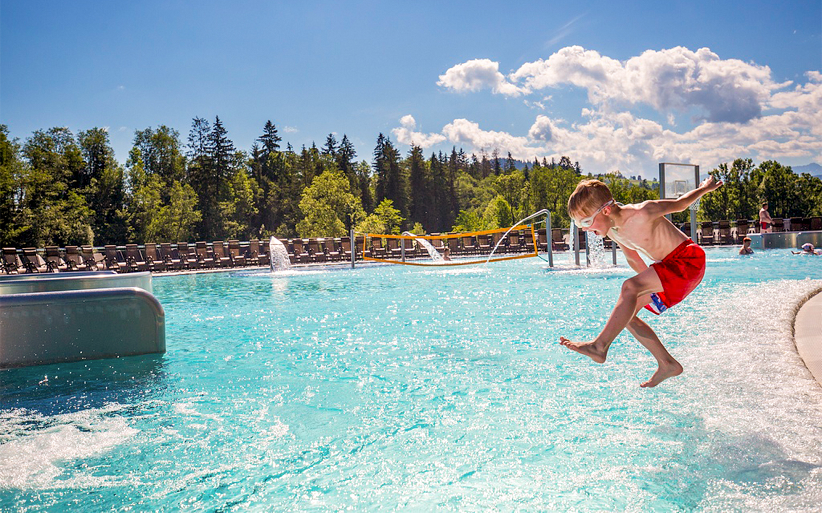 Child jumping into outdoor pool with forest backdrop, Zakopane, Poland.