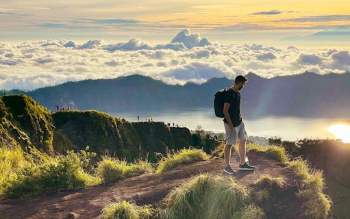 Man trekking Mount Batur at sunrise, overlooking clouds and distant peaks.