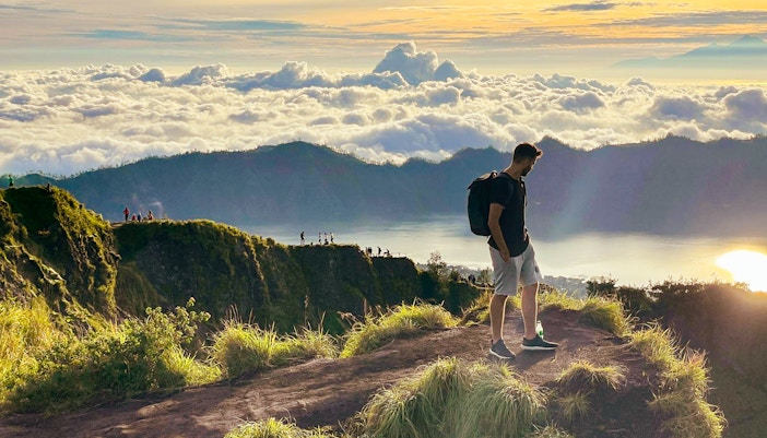 Man trekking Mount Batur at sunrise, overlooking clouds and distant peaks.
