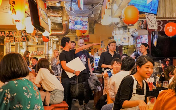 Patrons enjoying food and drinks at a bustling local izakaya bar in Japan.