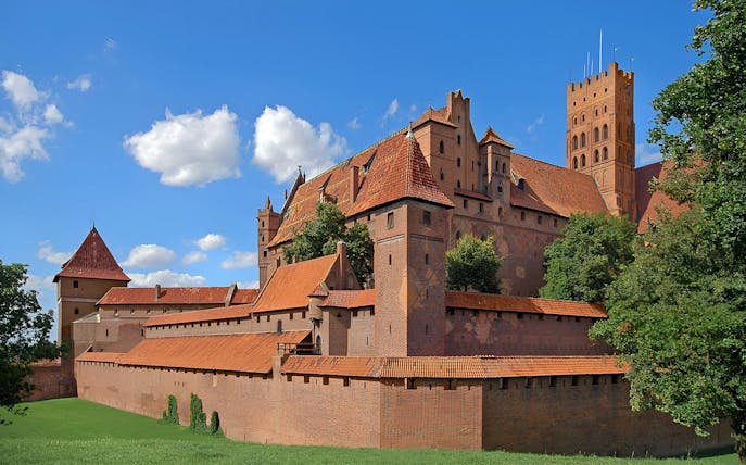 Malbork Castle with red brick walls and towers under a blue sky, viewed during audio guide tour from Gdańsk.