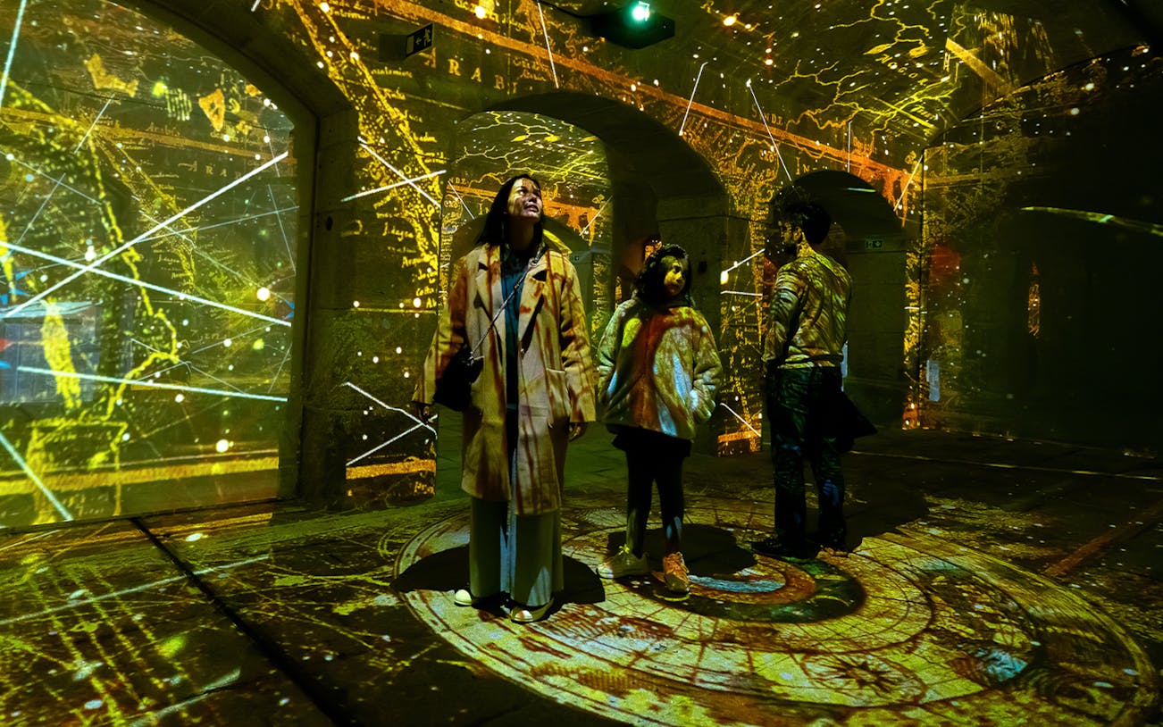 Visitors exploring Porto Legends exhibit with illuminated maps and projections.