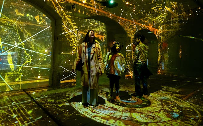 Visitors exploring Porto Legends exhibit with illuminated maps and projections.