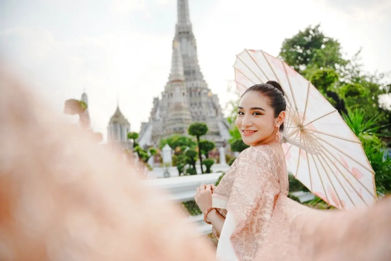 Woman in traditional Thai attire with parasol at Wat Arun, Bangkok.
