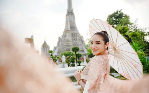 Woman in traditional Thai attire with parasol at Wat Arun, Bangkok.