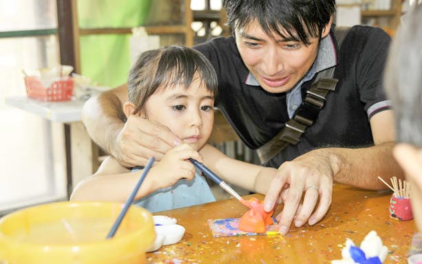 Child painting a figurine with guidance at Murasaki Mura Ryukyu Kingdom Theme Park.