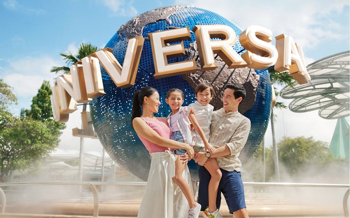 Family smiling in front of Universal Studios Singapore globe.