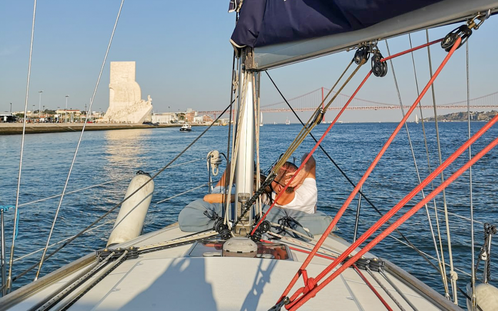 Tourist on Lisbon cruise boat viewing Monument of Discoveries and 25 de Abril Bridge.