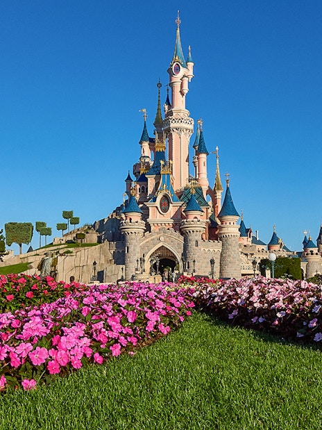 Sleeping Beauty Castle at Disneyland Paris with vibrant flower beds in the foreground.