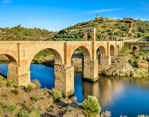 Alcántara Roman Bridge spanning the Tagus River in Toledo, surrounded by lush landscape.