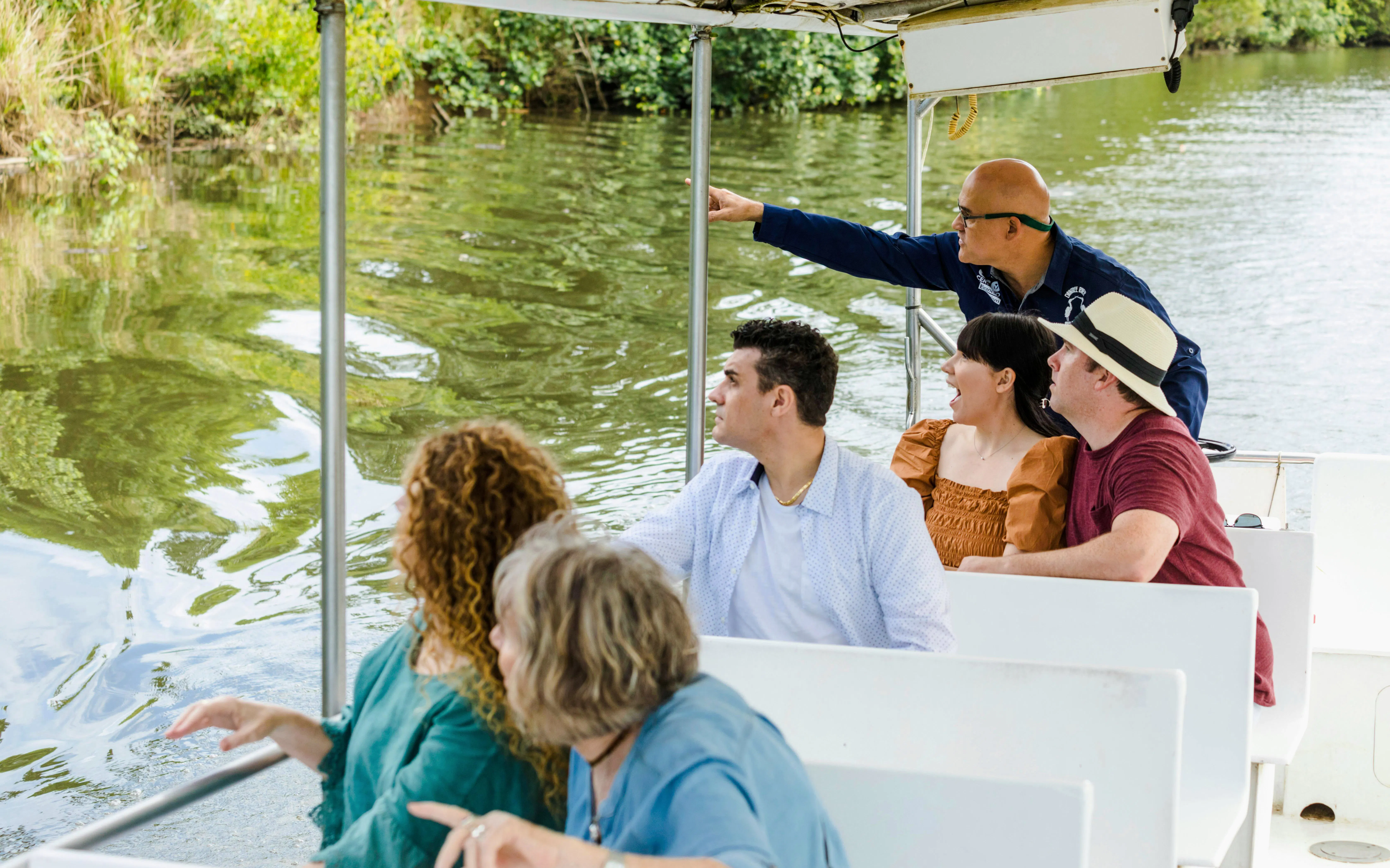 Tourists on a boat tour in Daintree Rainforest, guide pointing at wildlife.