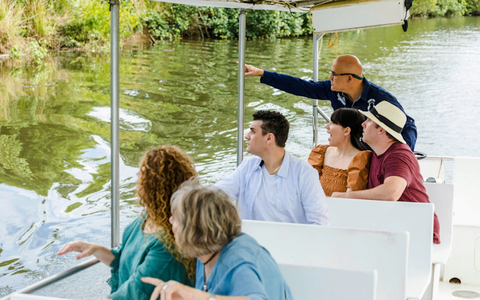 Tourists on a boat tour in Daintree Rainforest, guide pointing at wildlife.