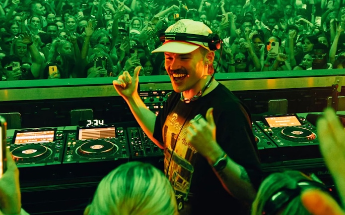 DJ performing at a lively Dom Dolla event in Ibiza with a cheering crowd.