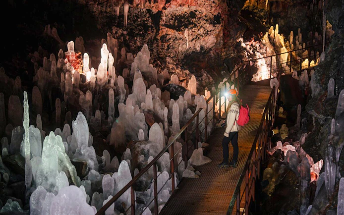 Guests walking through Raufarhólshellir Lava Tunnel surrounded by ice formations.