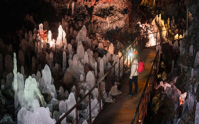Guests walking through Raufarhólshellir Lava Tunnel surrounded by ice formations.