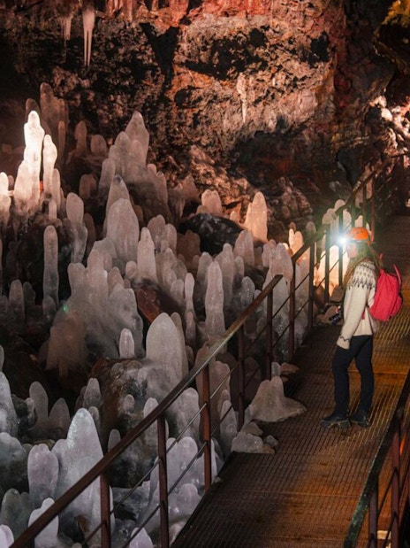 Guests walking through Raufarhólshellir Lava Tunnel surrounded by ice formations.