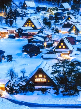 Traditional gassho-zukuri houses in snow-covered Shirakawa-go village, Japan, illuminated at dusk.