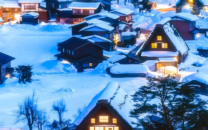 Traditional gassho-zukuri houses in snow-covered Shirakawa-go village, Japan, illuminated at dusk.