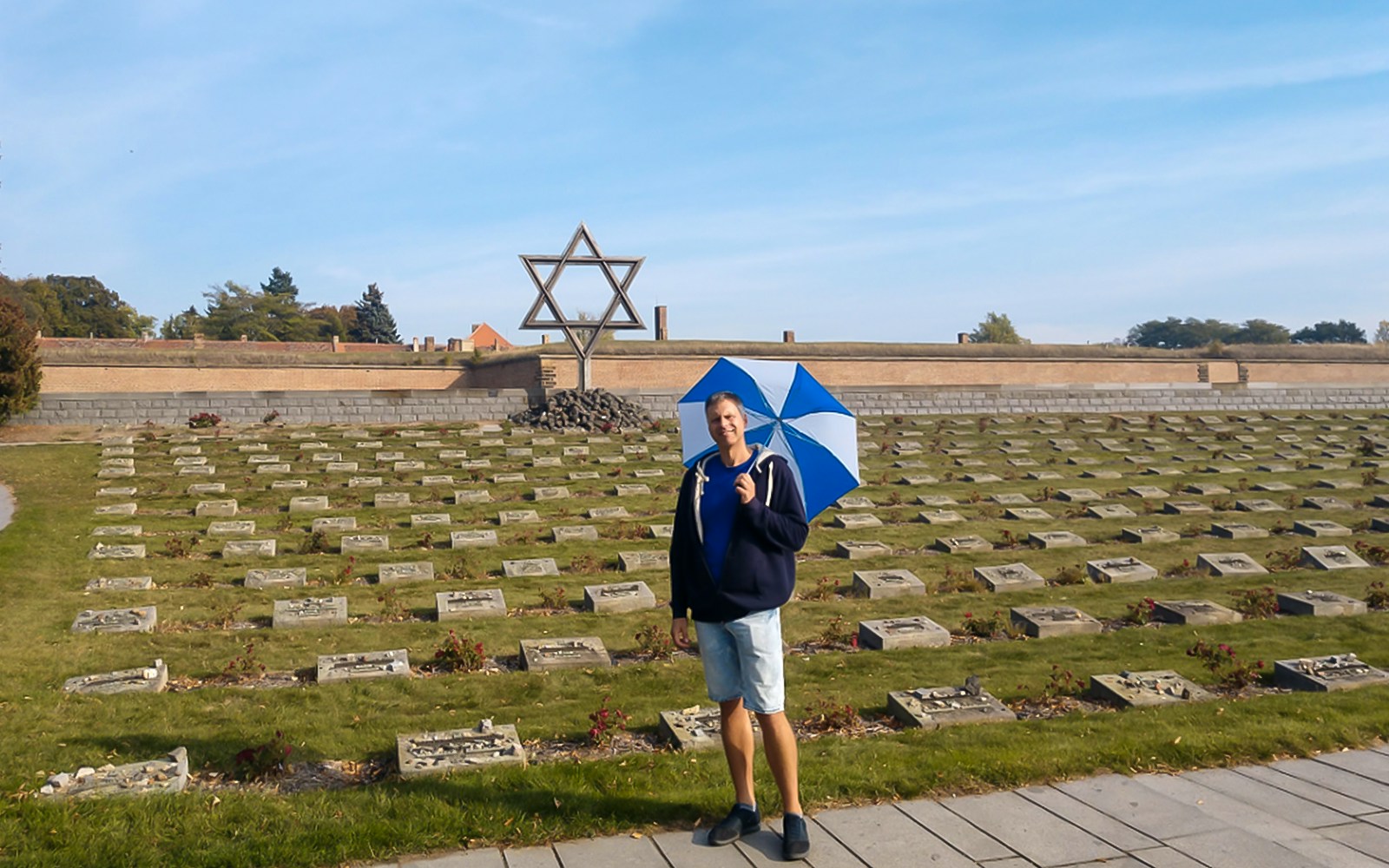 Tour guide with umbrella at Terezin Concentration Camp cemetery, large Star of David in background.
