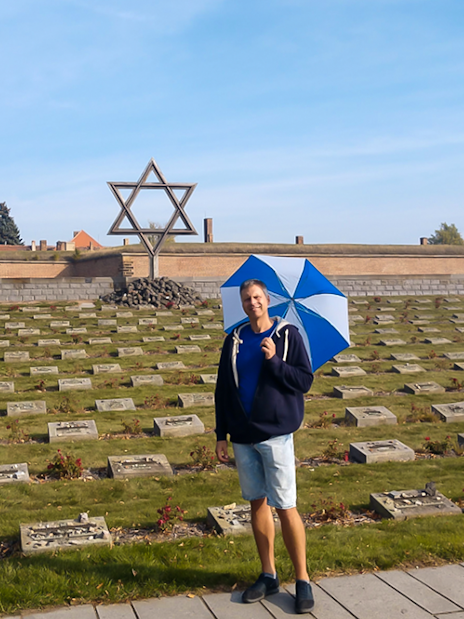 Tour guide with umbrella at Terezin Concentration Camp cemetery, large Star of David in background.