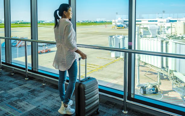 Woman with suitcase viewing runway at Don Mueang Airport, Bangkok, Thailand.