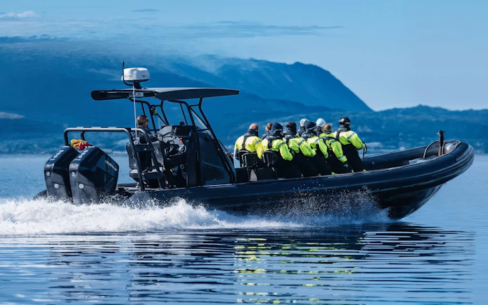 High-speed RIB boat with passengers in safety gear on open water.