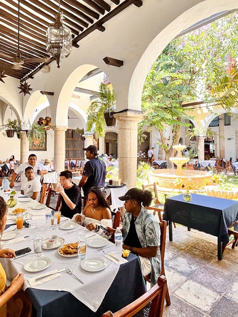 Dining area at Hotel Mesón del Marqués in Valladolid, Yucatán, with guests seated near a courtyard fountain.