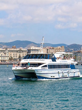 Las Golondrinas boat tour in Barcelona harbor with cityscape in background.