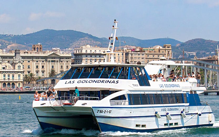 Las Golondrinas boat tour in Barcelona harbor with cityscape in background.