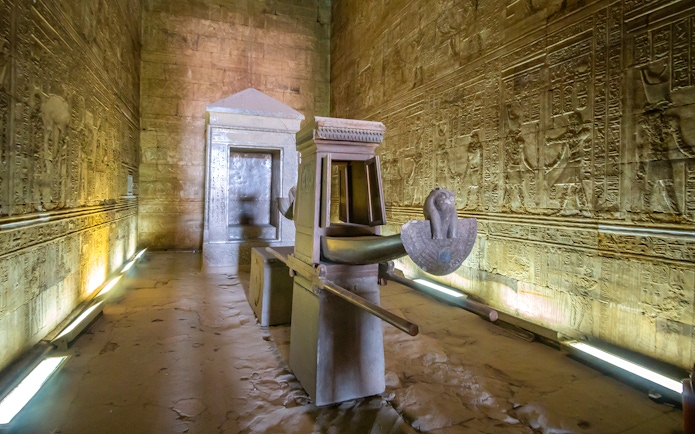 Sacred boat of Pharaoh in the Temple of Horus at Edfu, surrounded by hieroglyphic walls.