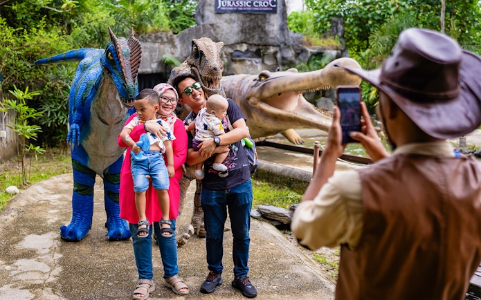 Family posing with dinosaur statues at Crocodile Adventureland Langkawi.