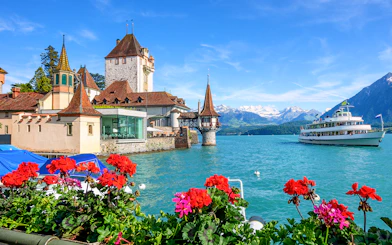 Oberhofen Castle on Lake Thun with a boat and Alps in the background, Switzerland.