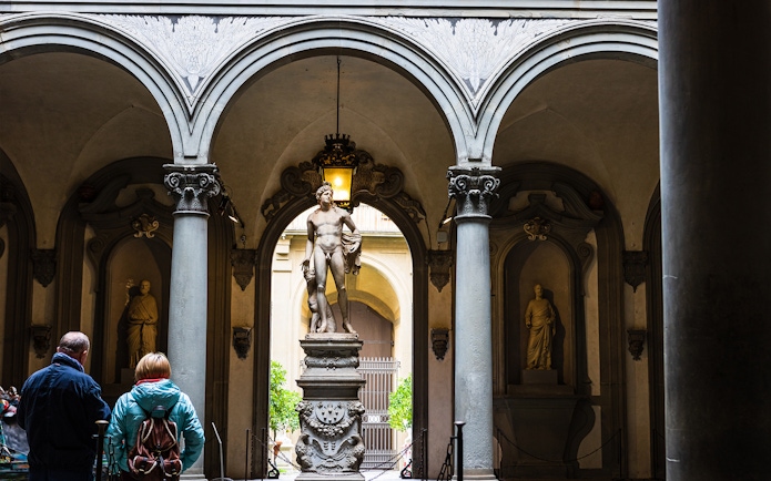 Visitors view a marble statue through arches at Uffizi Gallery, Florence.