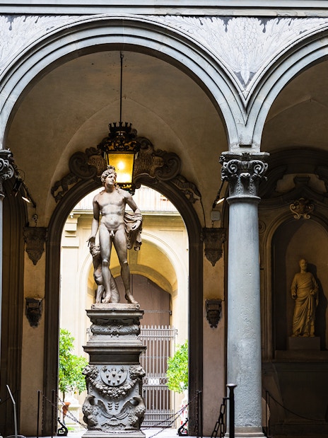 Visitors view a marble statue through arches at Uffizi Gallery, Florence.