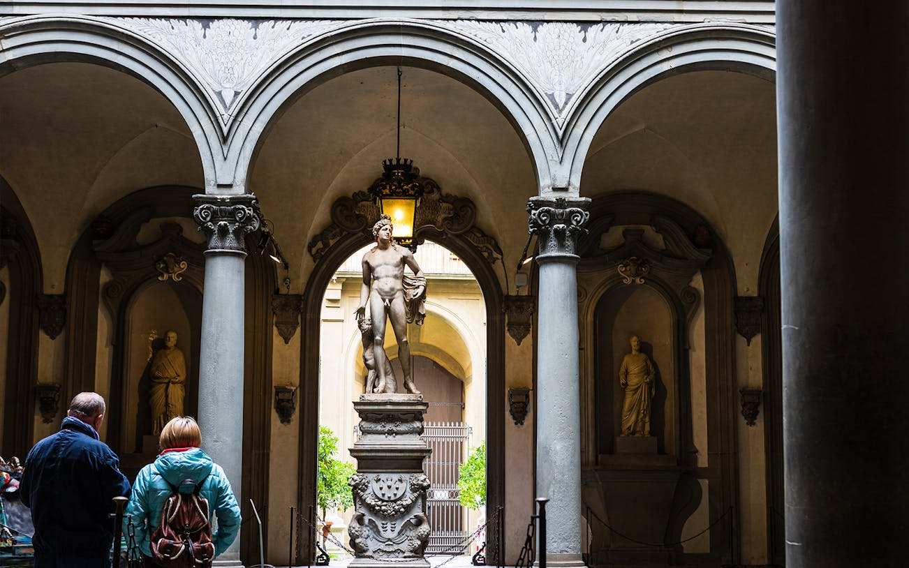 Visitors view a marble statue through arches at Uffizi Gallery, Florence.