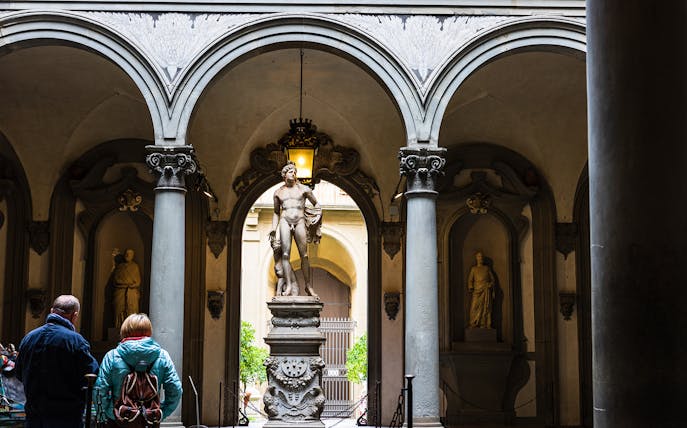 Visitors view a marble statue through arches at Uffizi Gallery, Florence.