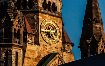 Kaiser Wilhelm Memorial Church clock tower in Berlin at dusk.