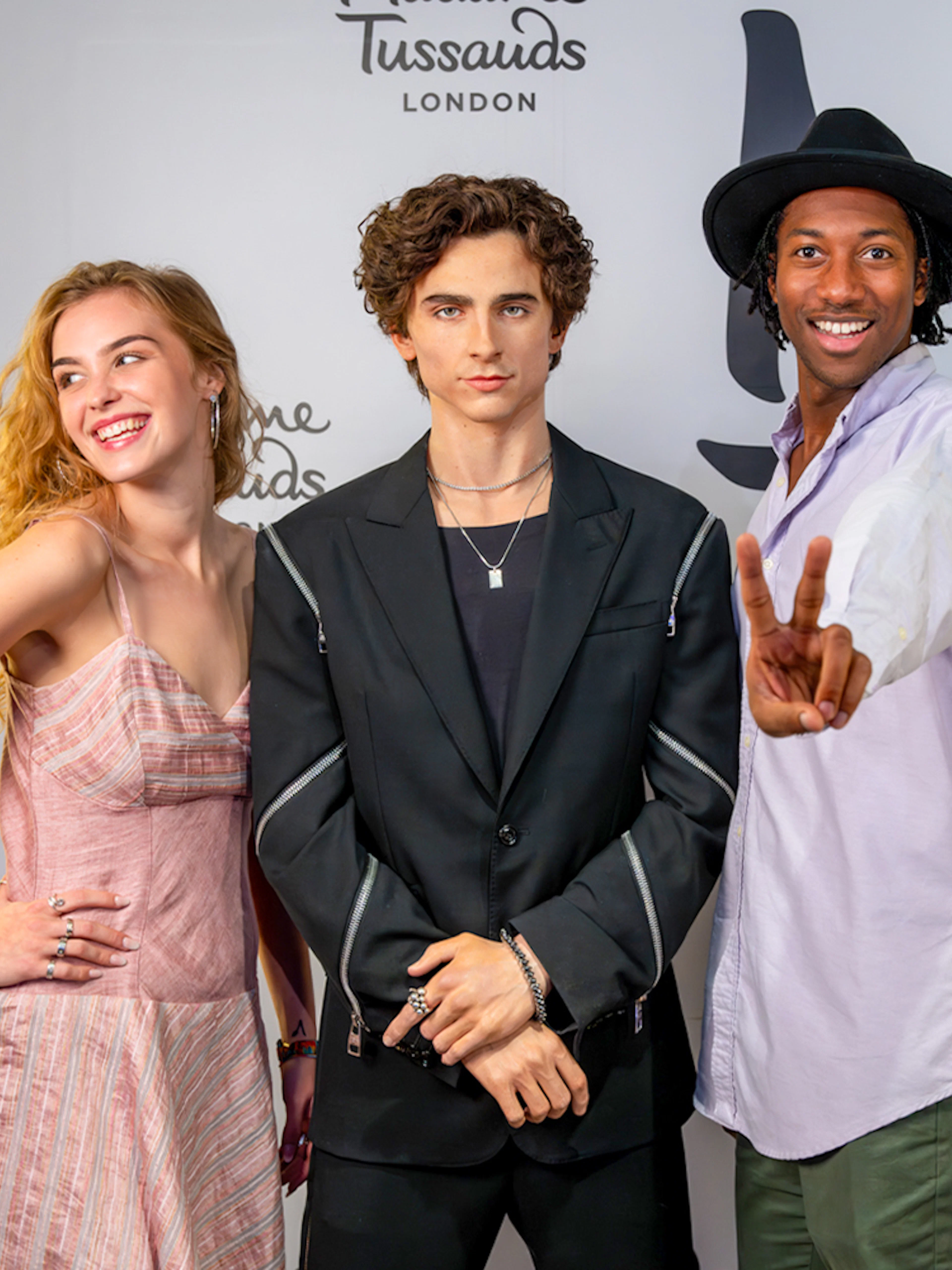 Wax figure of a celebrity at Madame Tussauds London with three visitors posing.
